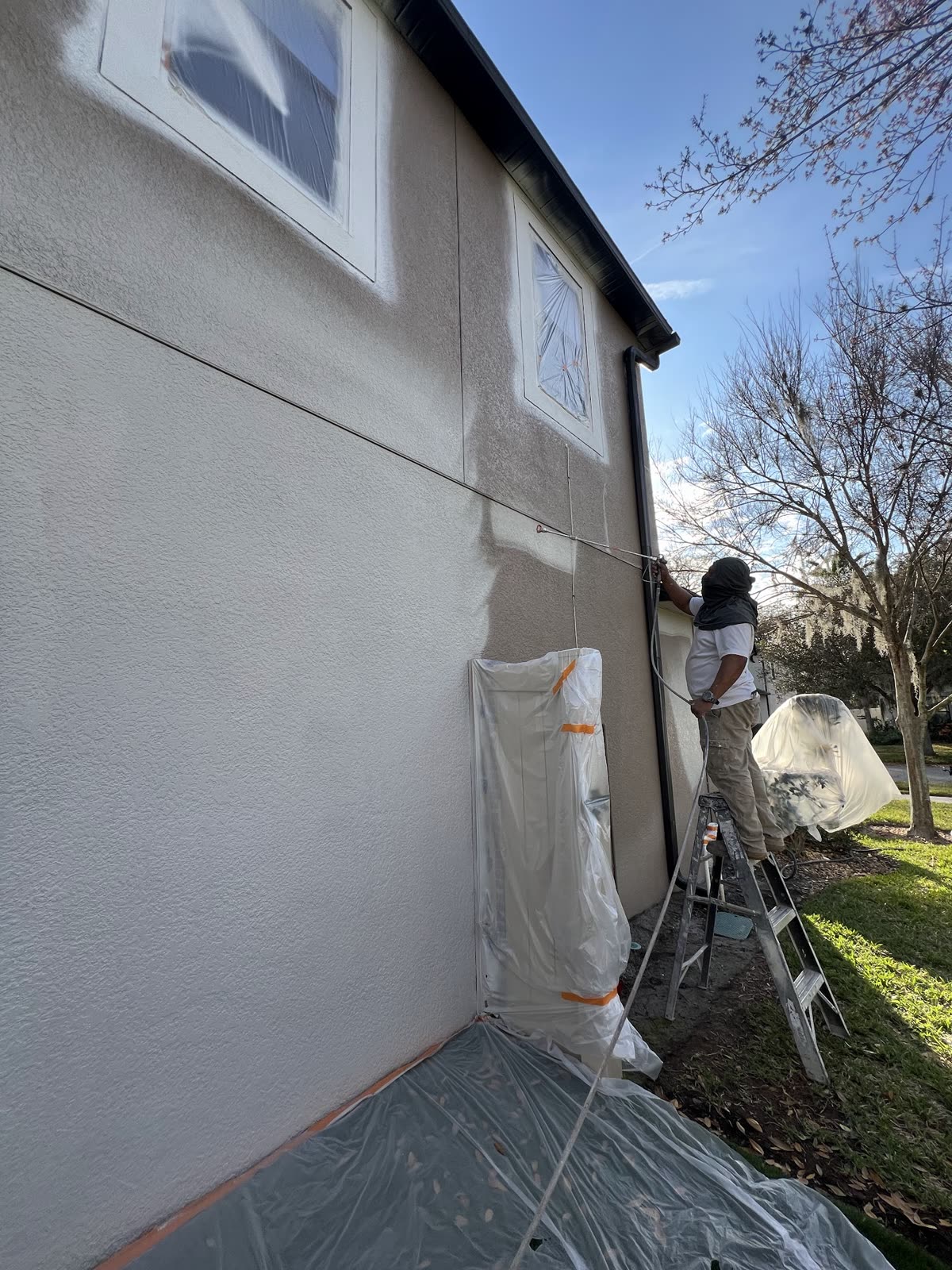Painter spray-painting an exterior stucco wall